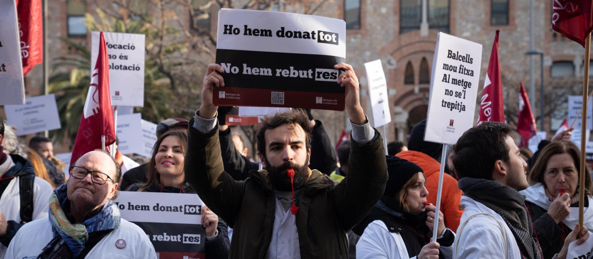 Varias personas protestan con pancartas y batas blancas durante una manifestación del sindicato médico Médicos de Cataluña por la huelga sanitaria, a 25 de enero de 2023, en Barcelona