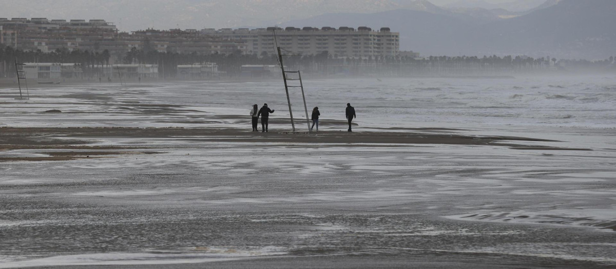 Cuatro personas pasean por la playa de la Malvarrosa cuando la Aemet ha establecido para este martes la alerta naranja en las tres provincias de la Comunitat, por fenómenos costeros en el litoral de Valencia y la costa norte de Alicante, y por nieve y precipitaciones de hasta 100 litros por metro cuadrado en el interior de Castellón. EFE/Manuel Bruque