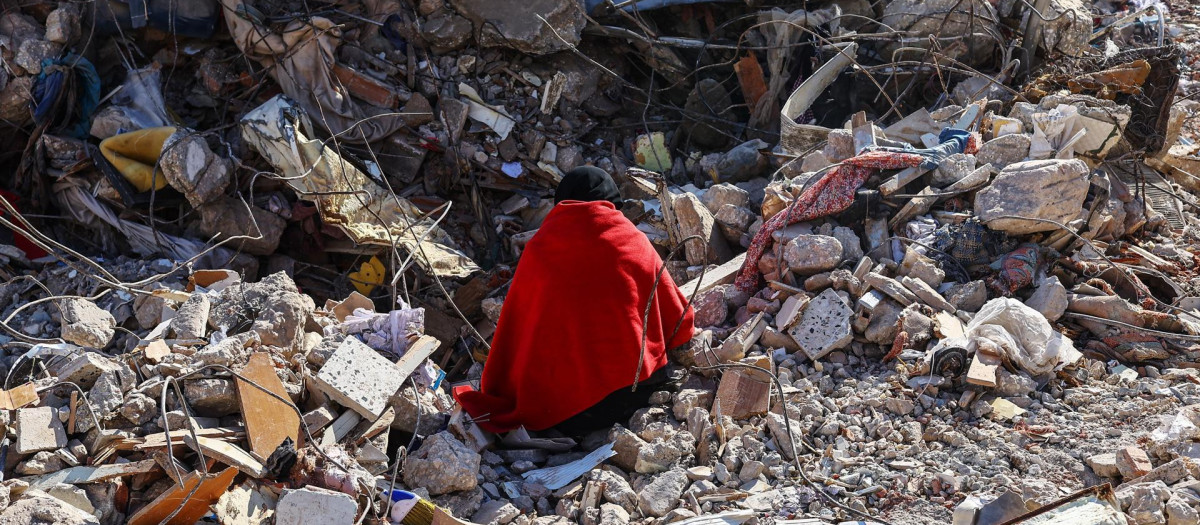 Una mujer sentada sobre los escombros de su casa