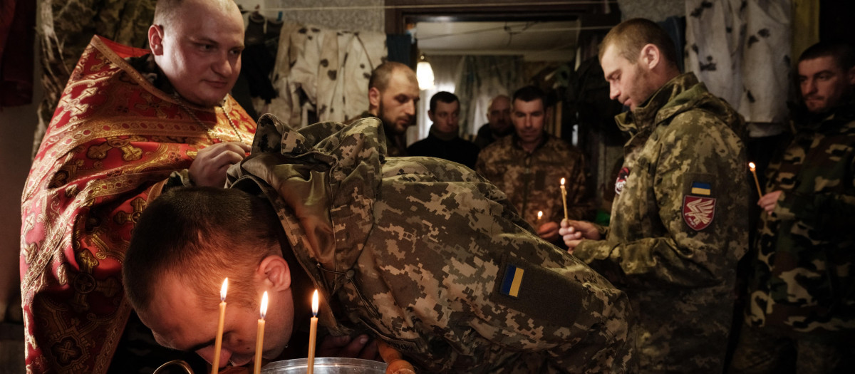 Mykola Berezyk (L), 28-year-old, chaplain to the Ukrainian Armys 95th Air Assault Brigade, also known as "Father Mykola, conducts a prayer for Ukrainian servicemen who returned from the frontline, as a serviceman kisses a cross in the Donetsk region on February 22, 2023, amid the Russian invasion of Ukraine. (Photo by YASUYOSHI CHIBA / AFP)