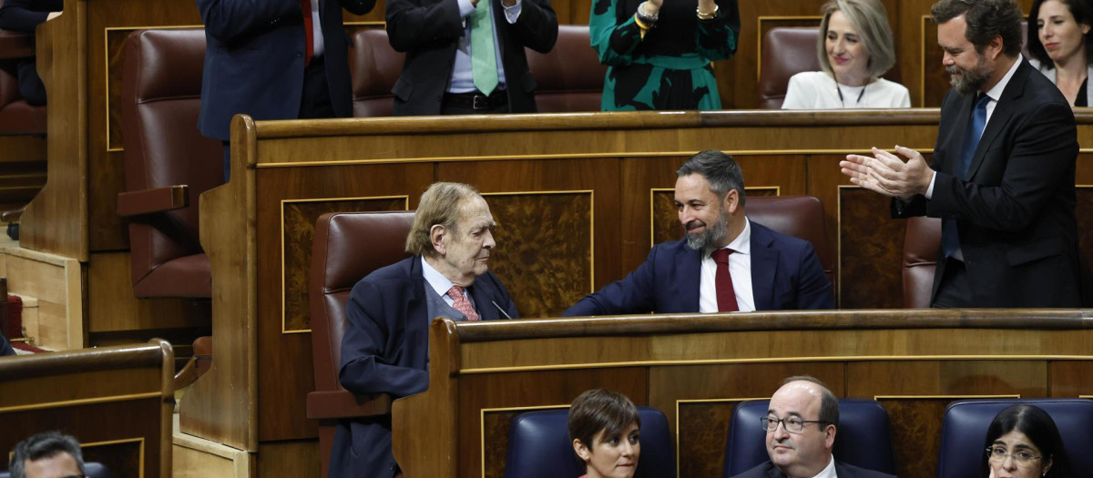 El profesor Ramón Tamames (i), acompañado por el líder de Vox, Santiago Abascal (c), mientras recibe los aplausos de los diputados de la formación política tras intervenir durante la segunda y última jornada del debate de la moción de censura que impulsa Vox, con Ramón Tamames de candidato, contra el Gobierno del socialista Pedro Sánchez, este miércoles en el Congreso de los Diputados