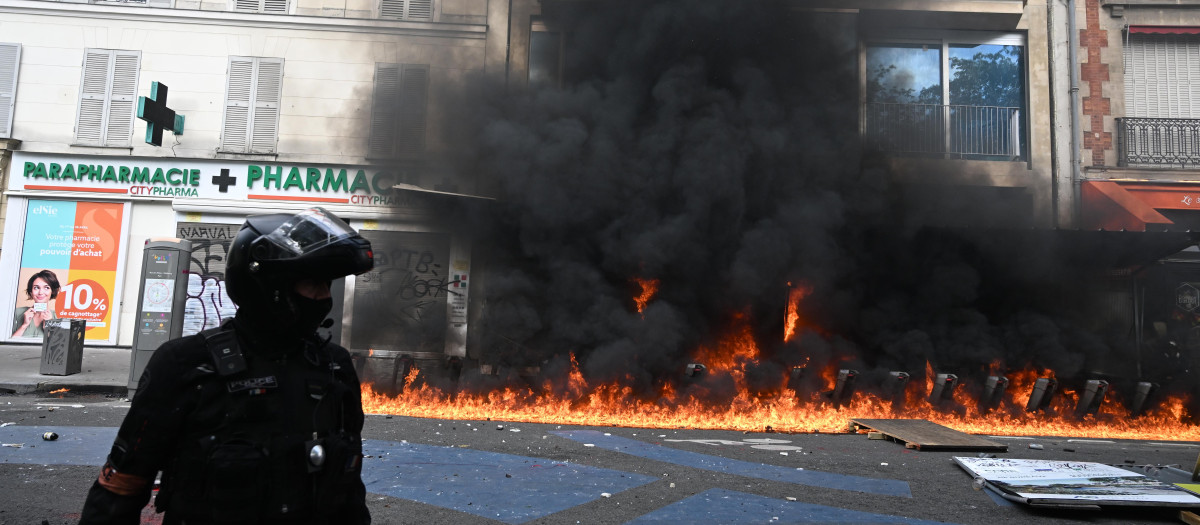 Un agente de Policía junto a una estación de bicicletas públicas ardiendo en París