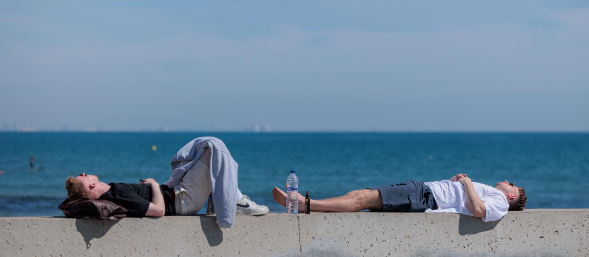 Dos personas descansan al sol en la playa de la Malvarrosa durante este segundo día de mayo en el que se mantienen las altas temperaturas