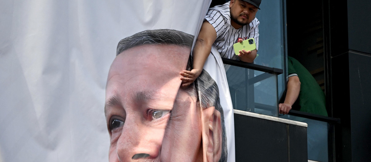 A local resident watches the Turkish President's speech next to a banner with his portrait during a rally in the Beyoglu district on the eve of the presidential and parliamentary elections, on the European side of Istanbul, on May 13, 2023. Erdogan warned his conservative supporters they could face reprisals should his secular rival rise to power in momentous weekend polls. Erdogan has been trying to rally his base ahead of elections that put his Islamic style of rule in the largest Muslim-majority member of NATO on the line. (Photo by OZAN KOSE / AFP)