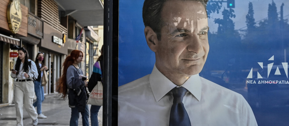 Varios jóvenes griegos caminan junto a un cartel de la campaña de el primer ministro griego y candidato oficialista Kyriakos Mitsotakis