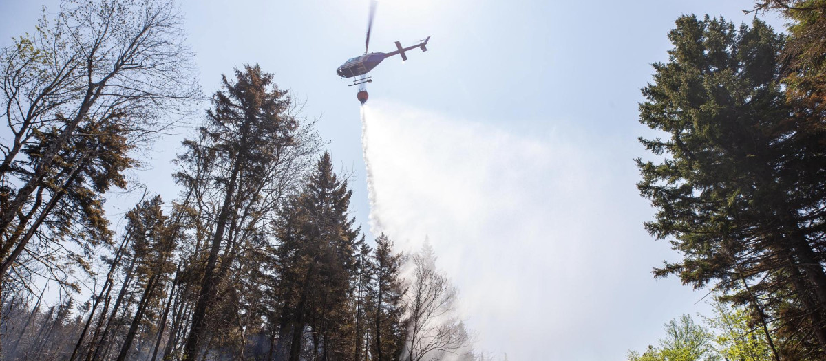 Un helicóptero arroja agua mientras una excavadora hace un cortafuegos en el incendio forestal de Tantallon en Tantallon, Nueva Escocia, Canadá