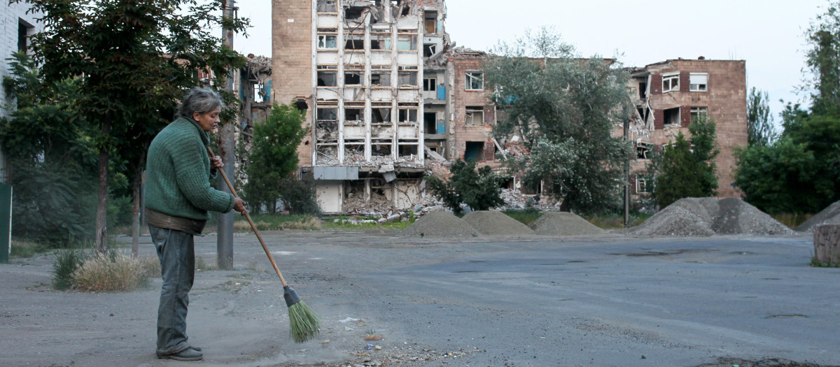Una mujer limpia una calle frente a un edificio destruido en la ciudad portuaria de Mariupol, en el mar de Azov, controlada por Rusia