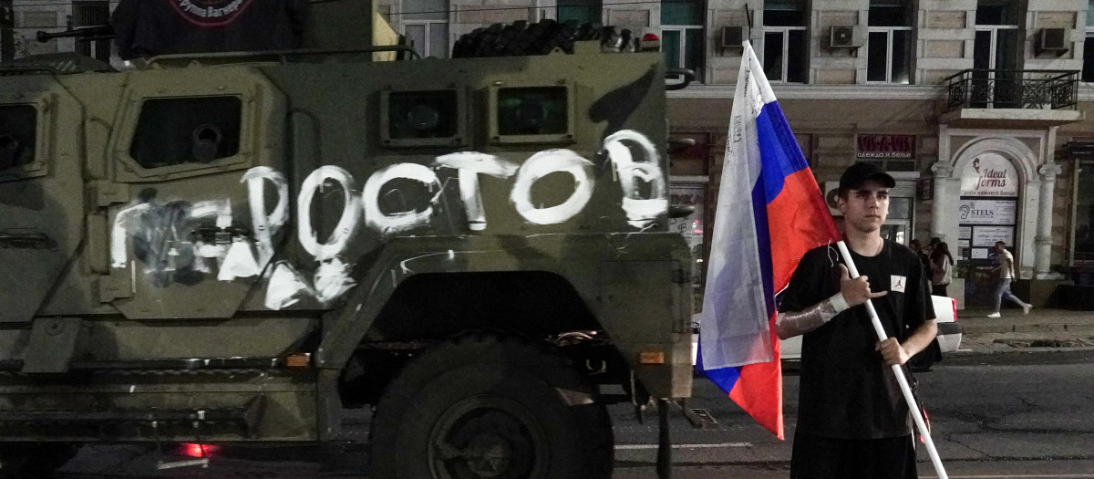 Un hombre sostiene la bandera nacional rusa frente a un vehículo militar del grupo Wagner con el cartel que dice Rostov