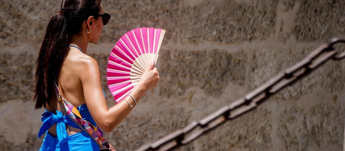 Una  turista, con un abanico en la mano por los alrededores de la Catedral de Sevilla