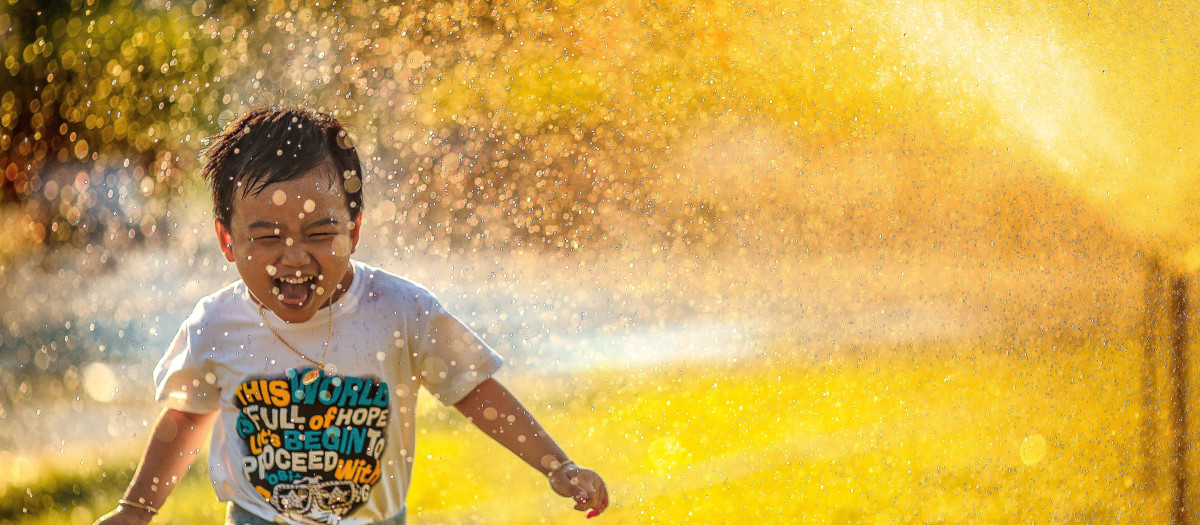 Un niño corre entre los aspersores