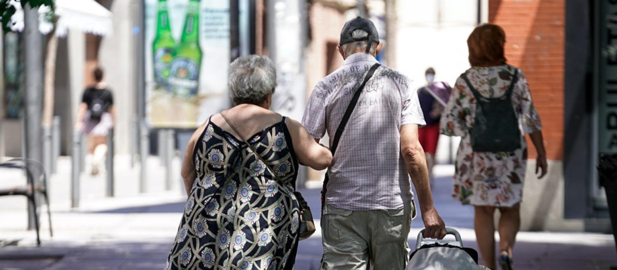Una pareja de ancianos camina por la calle con un carro de compra.