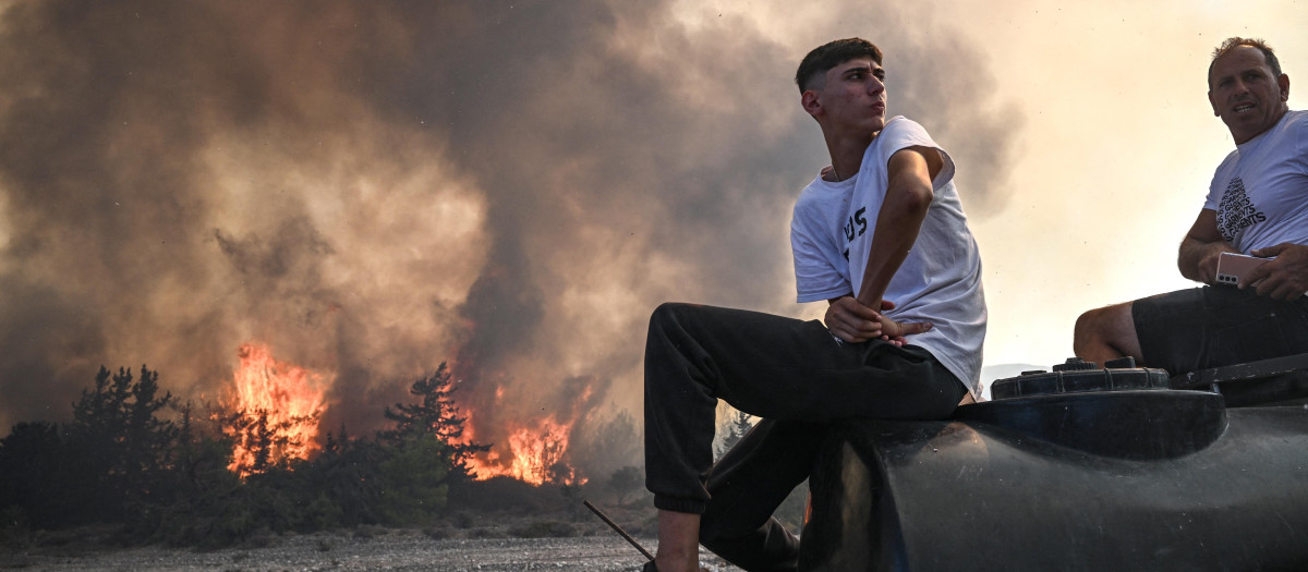 Dos hombres sentados en su camioneta mientras los incendios forestales devoran la isla de Rodas