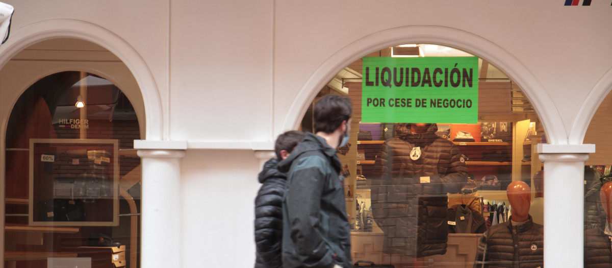 Dos personas pasan por delante de un establecimiento abierto donde se puede leer "Liquidación por cese de negocio"