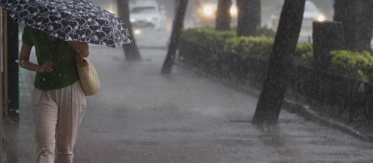 Una mujer camina por la acera bajo una intensa lluvia en Valencia