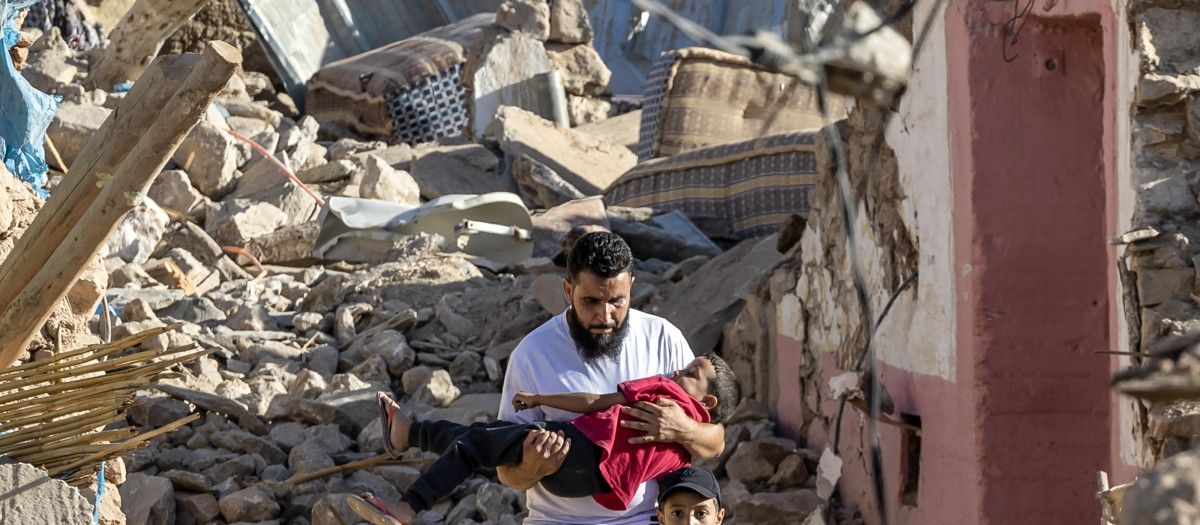 Un hombre carga a un niño mientras pasa junto a casas destruidas, en Marrakech
