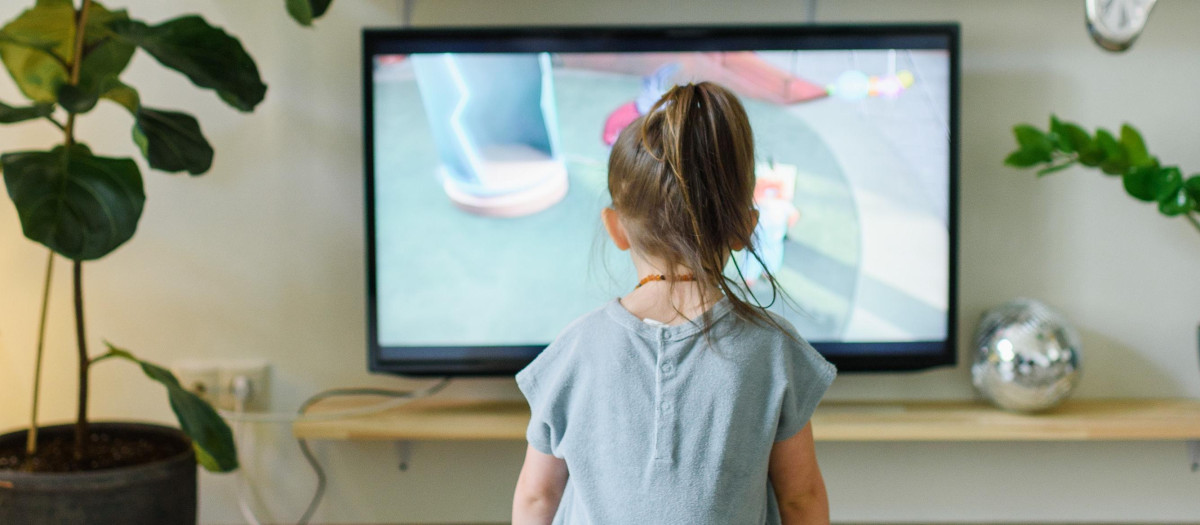 Una niña pequeña frente a un televisor encendido