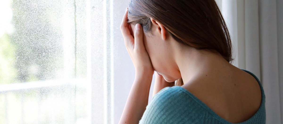 Sad depressed girl crying near the window at home in a rainy day, focus on model hand, indoor picture