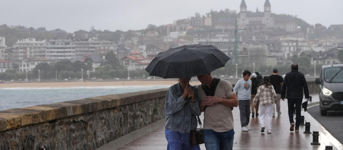 Dos personas se protegen de la lluvia con un paraguas en la playa de Ondarreta, San Sebastián