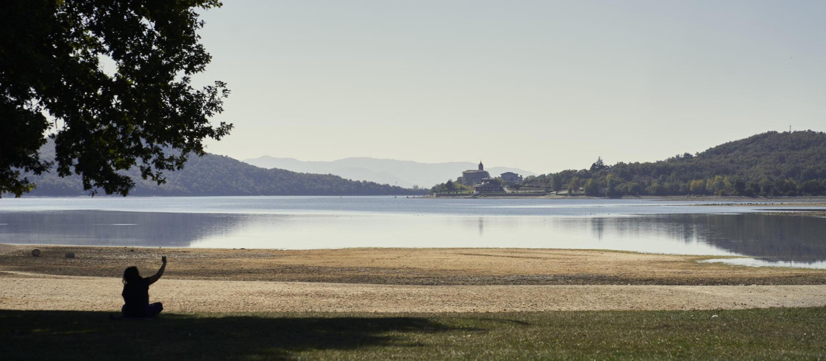 Una mujer se resguarda del sol bajo un árbol en la playa de Garaio del pantano de Ullibarri de Gamboa, en Álava