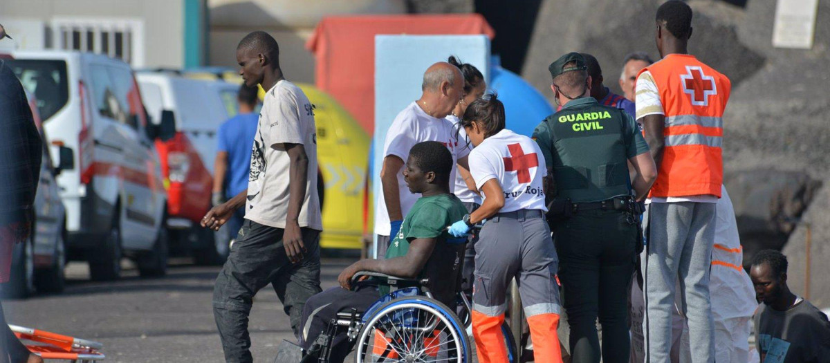 Una trabajadora de la Cruz Roja traslada en silla de ruedas a uno de los inmigrantes llegados en cayuco al puerto de El Hierro (Santa Cruz de Tenerife)