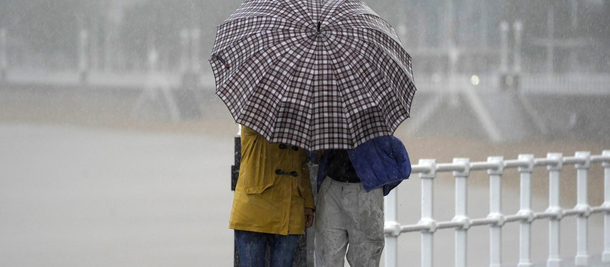 Dos personas comparten paraguas bajo la lluvia en la Playa de San Lorenzo de Gijón