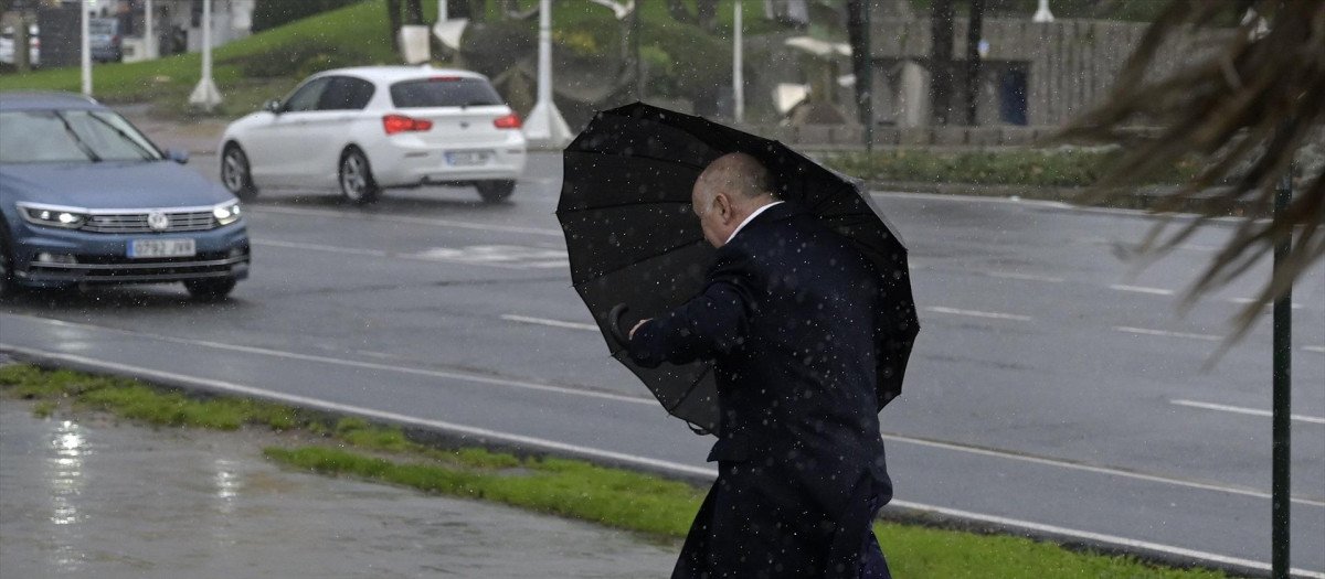 Un hombre con paraguas trata de refugiarse del viento y de la lluvia