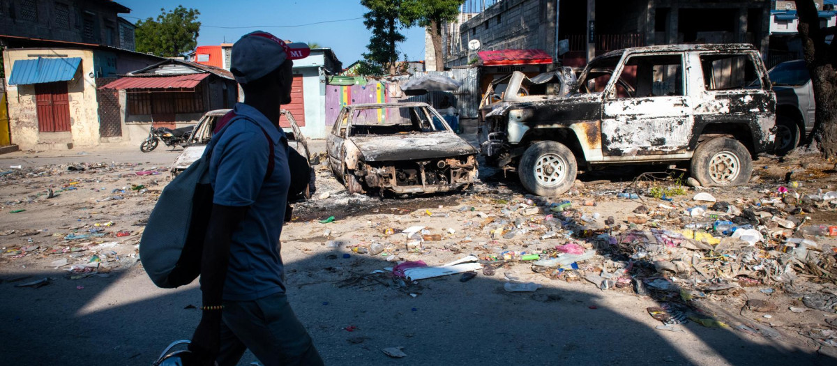 Un hombre camina frente a vehículos incinerados, este sábado en Puerto Príncipe