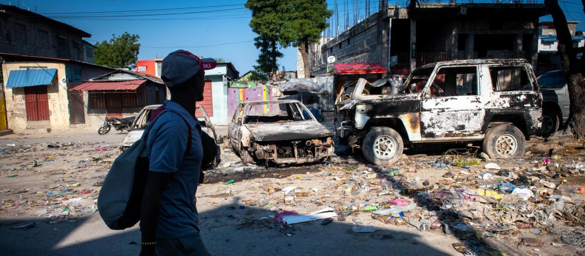 Un hombre camina frente a vehículos incinerados, este sábado en Puerto Príncipe