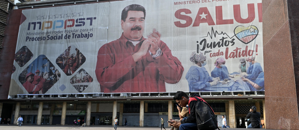 La gente camina frente a una enorme pancarta que representa al presidente venezolano, Nicolás Maduro, en Caracas