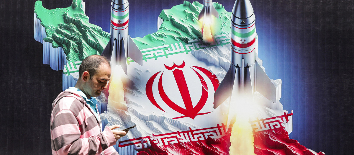 Un hombre pasa junto a una pancarta que representa misiles lanzados desde Irán, en Teherán