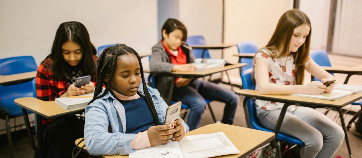 Niños mirando el móvil en un aula.