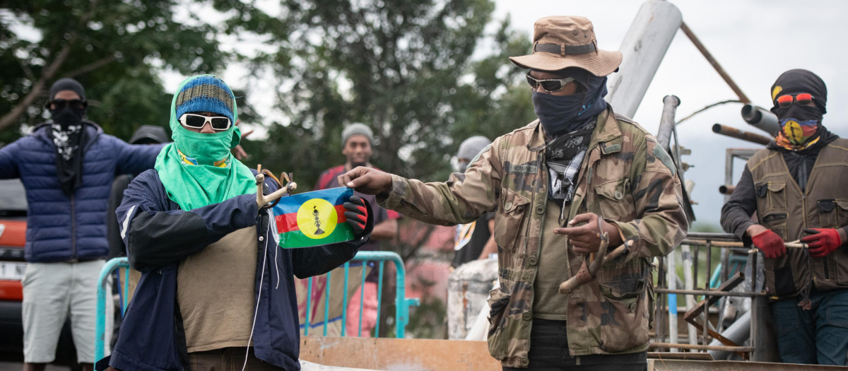 Transeúntes sostienen una bandera del Frente Socialista Kanaco de Liberación Nacional (FLNKS) en un control de carretera en Ducos, territorio francés de Nueva Caledonia en el PacíficoThe unrest has left six people dead, including two police, and hundreds injured. (Photo by Delphine Mayeur / AFP)