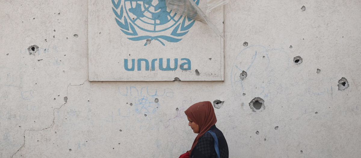 Una mujer palestina pasa junto a un muro dañado que lleva el logotipo de la UNRWA en un campamento para desplazados internos en Rafah, Gaza