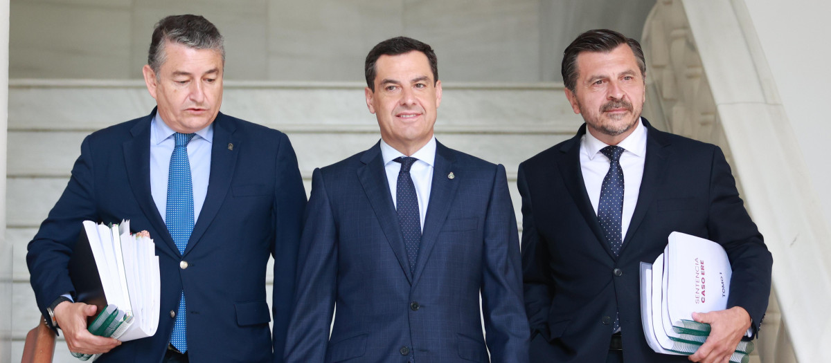 El presidente de la Junta, Juanma Moreno, escoltado por el consejero de la Presidencia, Antonio Sanz (izq.), y el portavoz parlamentario del PP andaluz, Toni Martín, con la sentencia del caso ERE bajo el brazo