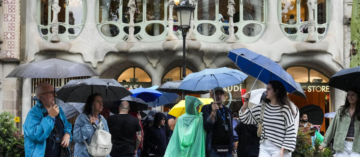 Varios turistas se protegen de la lluvia este lunes en las inmediaciones de la Casa Batlló del paseo de Gracia de Barcelona