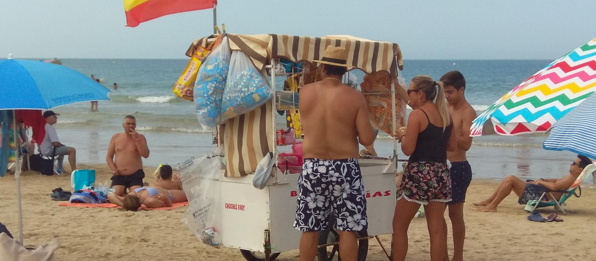 Un vendedor ambulante ofrece a los bañistas bebida fría o fruta fresca en la playa de Costa Ballena en Rota