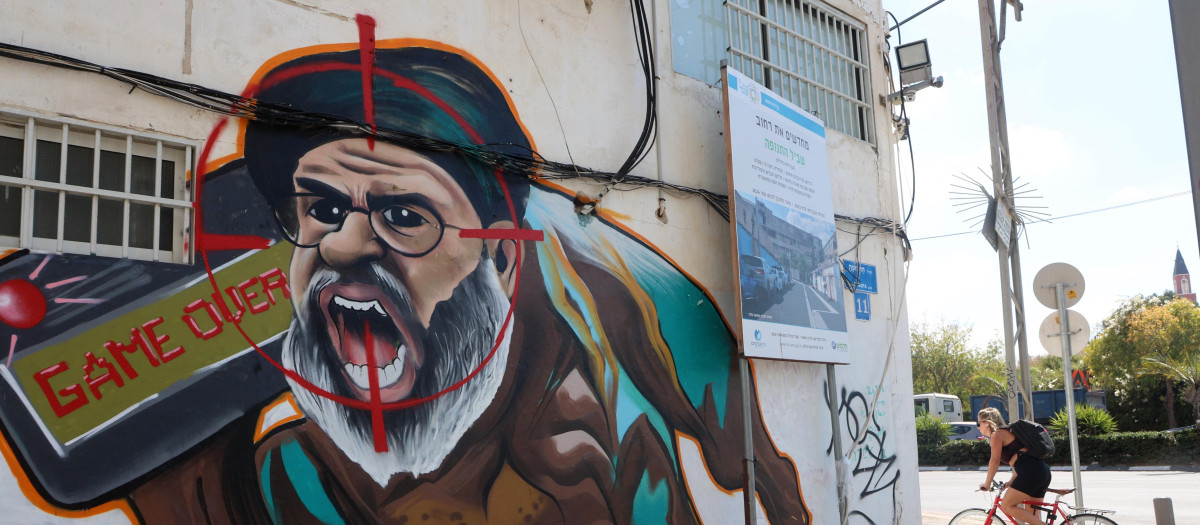 Un israelí pasa en bicicleta junto a un grafiti que representa a Hasan Nasralá, en Tel Aviv