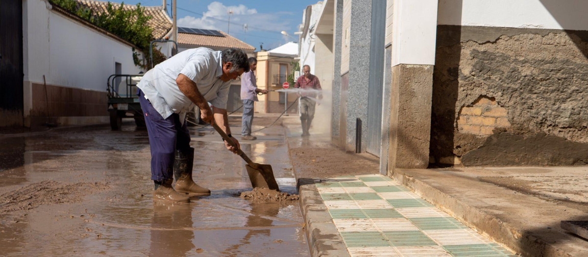 Un vecino limpia la puerta de su domicilio tras una inundación en un pueblo sevillano (archivo)
