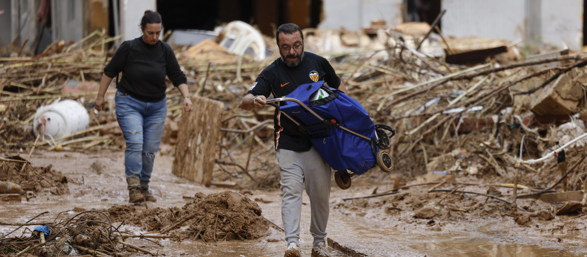 PAIPORTA (VALENCIA), 02/11/2024.- Un vecino lleva en volandas un carro de la compra entre el fango y restos en la localidad de Paiporta este sábado tras el paso de la DANA. EFE/ Biel Aliño