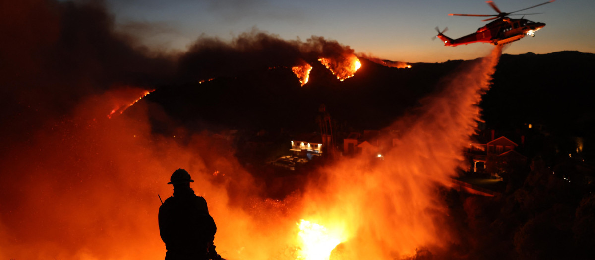 El personal de bomberos responde a las casas destruidas mientras un helicóptero arroja agua mientras el incendio Palisades crece en Pacific Palisades, California