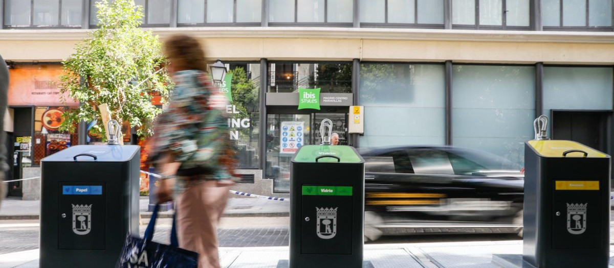 Viandante pasando por delante de unos contenedores de recogida de residuos en una calle de Madrid