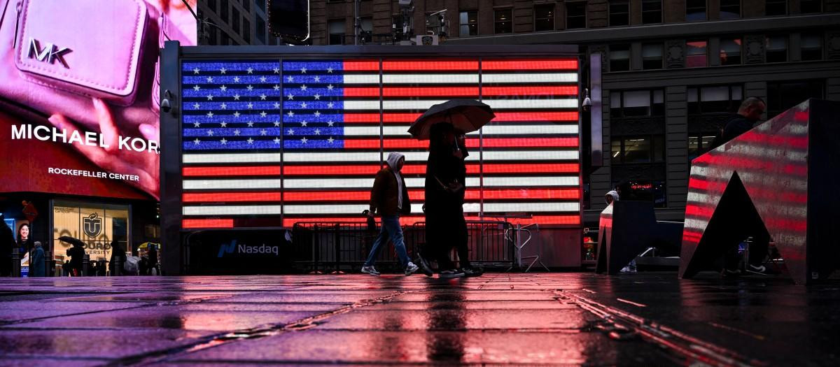 Un grupo de personas pasa junto a una bandera estadounidense en Times Square