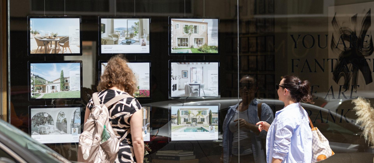 Dos personas observan los anuncios de viviendas en venta en una inmobiliaria.