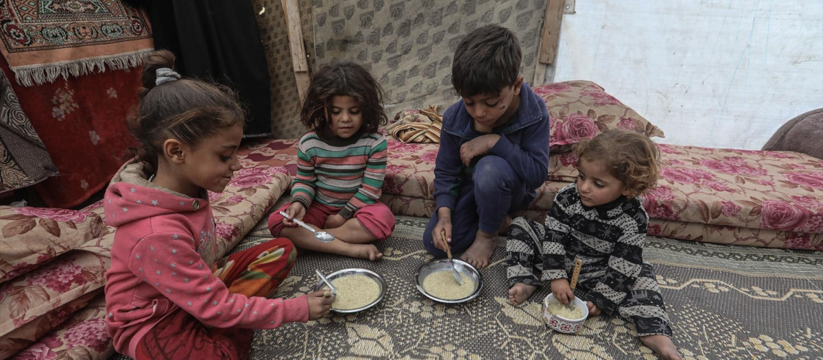 Niños palestinos comen alimentos entregados por una organización caritativa