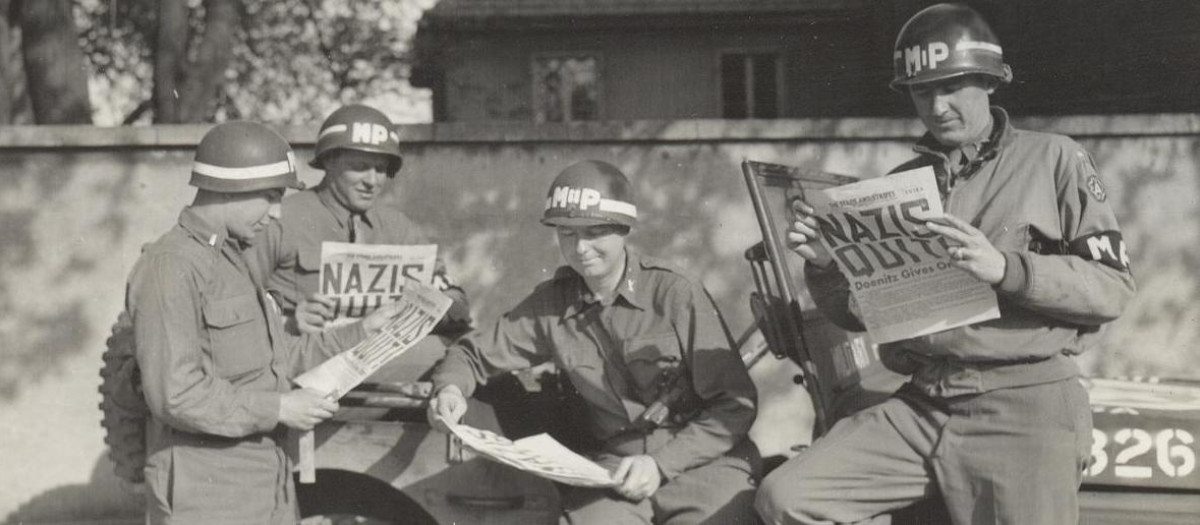 Policías militares de Estados Unidos leyendo sobre la rendición alemana en el periódico 'Stars and Stripes'.