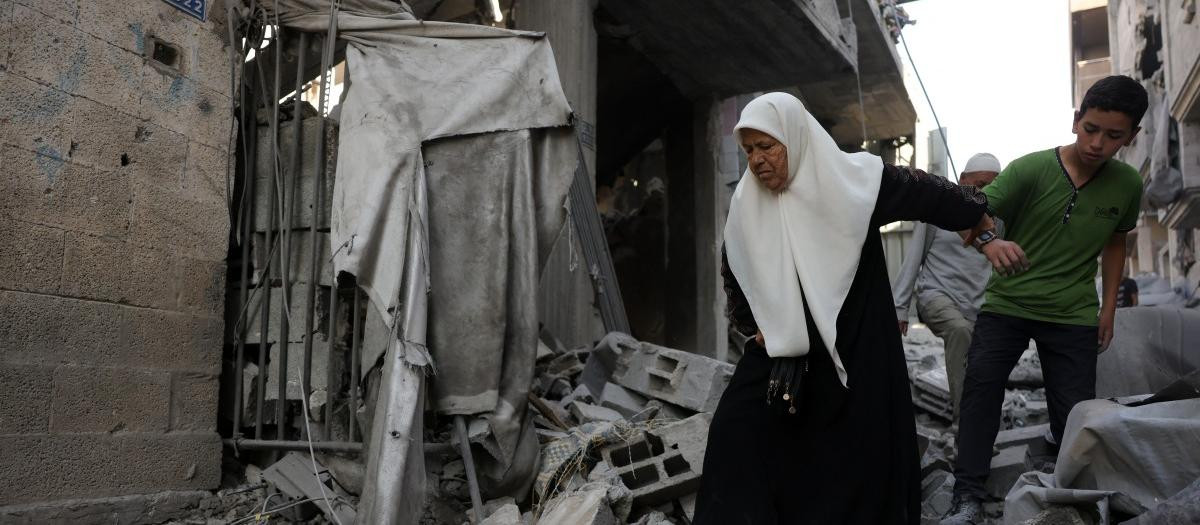 Un niño ayuda a una anciana palestina a caminar entre los escombros