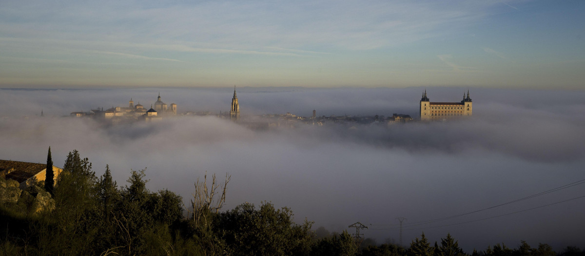 La niebla que cubre por completo el casco histórico de Toledo, a primera hora de la mañana, empieza a dejar ver el campanario de la catedral primada y el Alcázar de la ciudad. EFE/Ismael Herrero