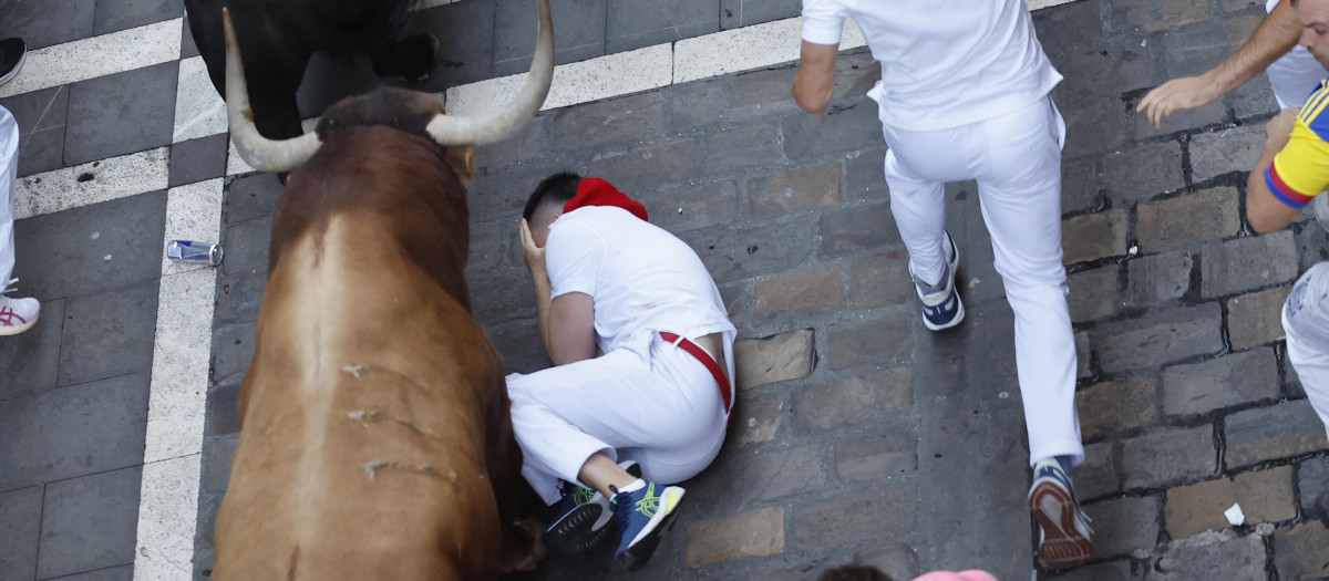 PAMPLONA, 10/07/2025.- Un mozo se intenta proteger tras caer al paso de los toros durante el cuarto encierro de los Sanfermines