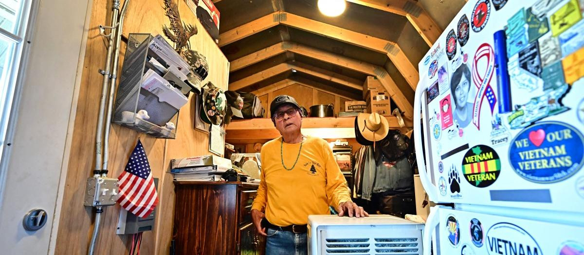 Navajo Nation resident and US veteran who gave his name as "Will" stands beside an air conditioner powered by a generator inside his tiny home which he calls a "tool shed" in Cameron, Arizona, on July 9, 2025 as he waits for electricity from the power grid to reach his residence. Initiatives like "Light Up Navajo," a project launched by the semi-autonomous government of the reservation in 2019, are connecting homes to the power grid with help from volunteer utility crews and federal funding but challenges remain due to the dispersed nature of the communities and vastness of the reservation. (Photo by Frederic J. BROWN / AFP)