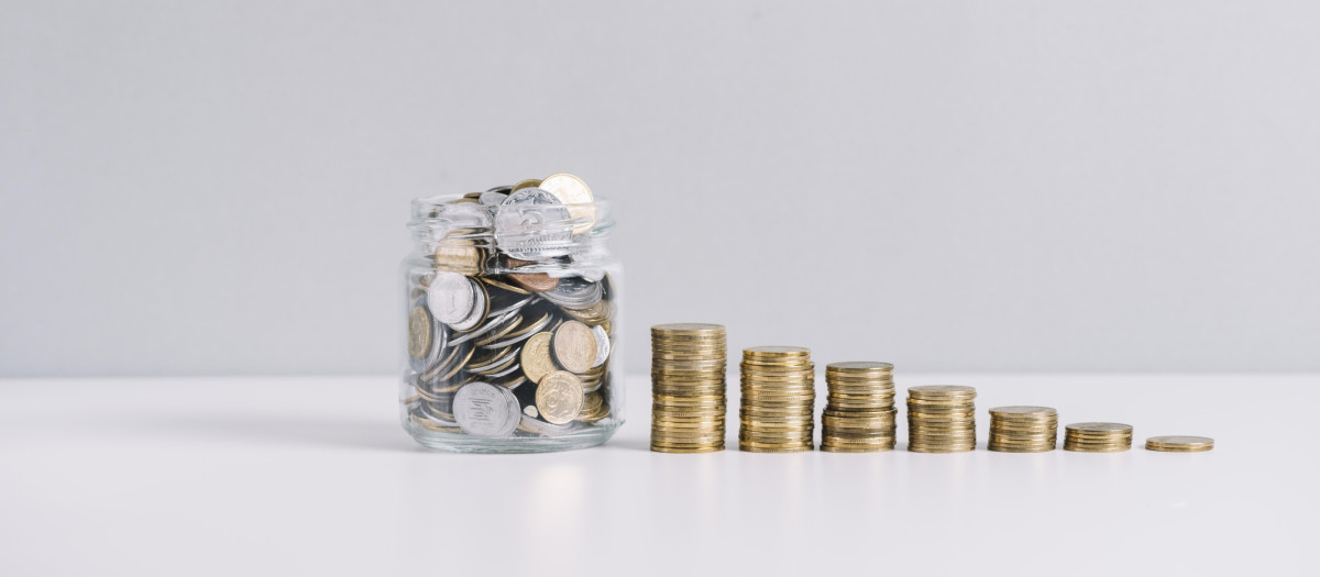 tarro de cristal lleno de dinero frente la disminucion de monedas apiladas sobre fondo blanco